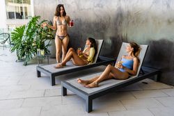 Two women are lounging in a courtyard, while the third is standing beside them. They are sipping on juices while chatting.