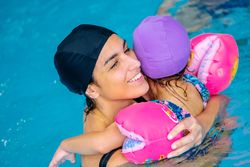 Cheerful girl swimming in pool with mother