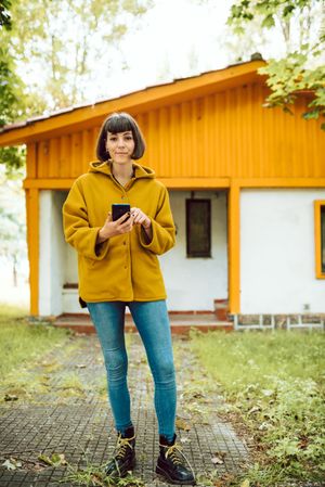 Smiling woman using smartphone near countryside house