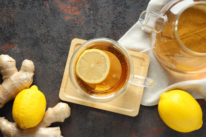 Cup and teapot with tea, lemon and ginger on gray background, top view