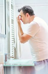 Man touching face in bathroom while looking in mirror