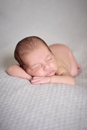 A naked newborn sleeping on her hands on top of a gray blanket