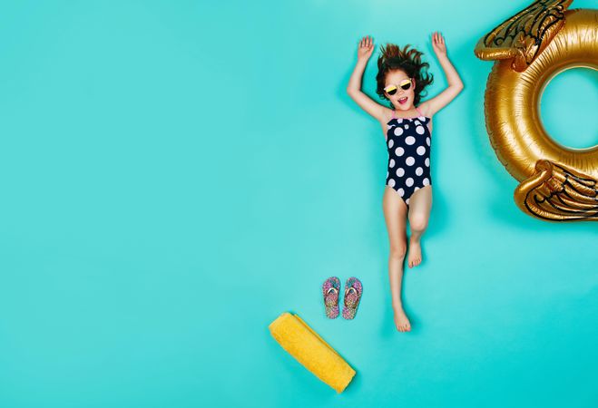 Happy girl in swimsuit and sunglasses lying on blue background