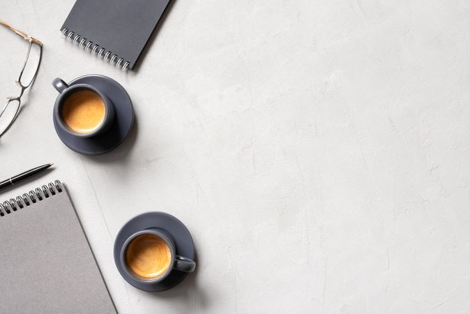 Top view of espresso, glasses and notepads on neutral desk