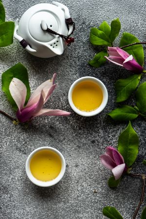 Top view of magnolia flowers with green tea and teapot on grey counter