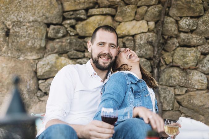 Laughing couple sitting on a terrace while bonding and enjoying a cup of wine