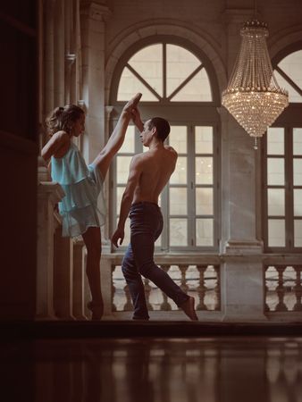 Ballet dancer raising leg of female partner in hall