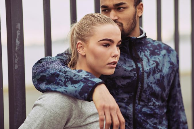 Beautiful woman standing next to her boyfriend as he looks away with his arm around her shoulder