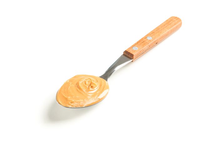 Creamy peanut butter in spoon isolated on light background. A traditional product of American cuisine