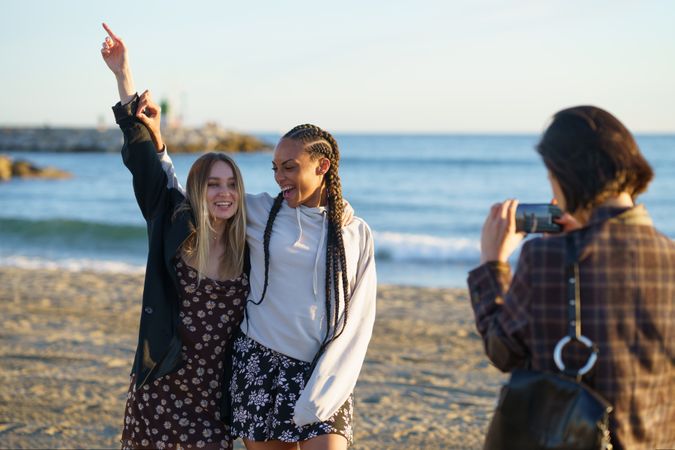 Happy girlfriends taking pictures together on beach at sunset