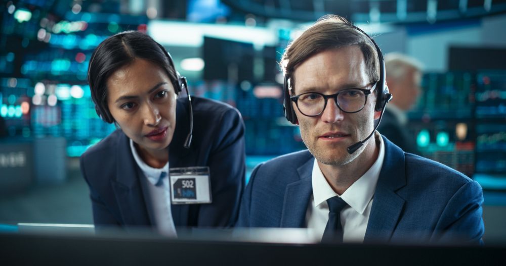 Two Successful Stock Exchange Traders Using Computer, Discussing Commodities Investments for an International Business Partner, Working in a Monitoring Center with Multiple Computer Screens