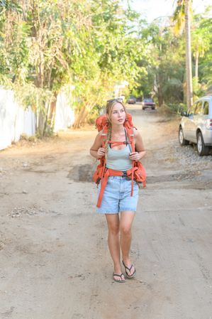 Young traveling woman walking along dirty road with backpack