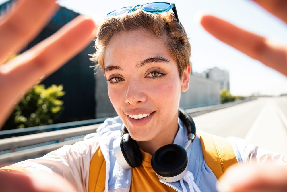 Playful trendy woman on street in sunshine covering camera with hands