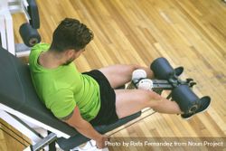 Top view of fit male in green t-shirt working out using leg extension machine, copy space 48z8Y0