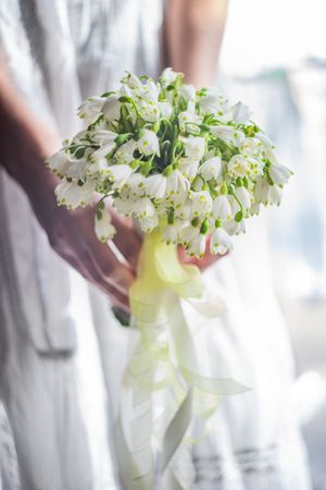 Hands of bridge holding floral bouquet with snowdrops
