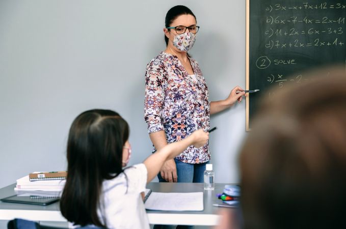 Teacher with mask explaining exercises in math class