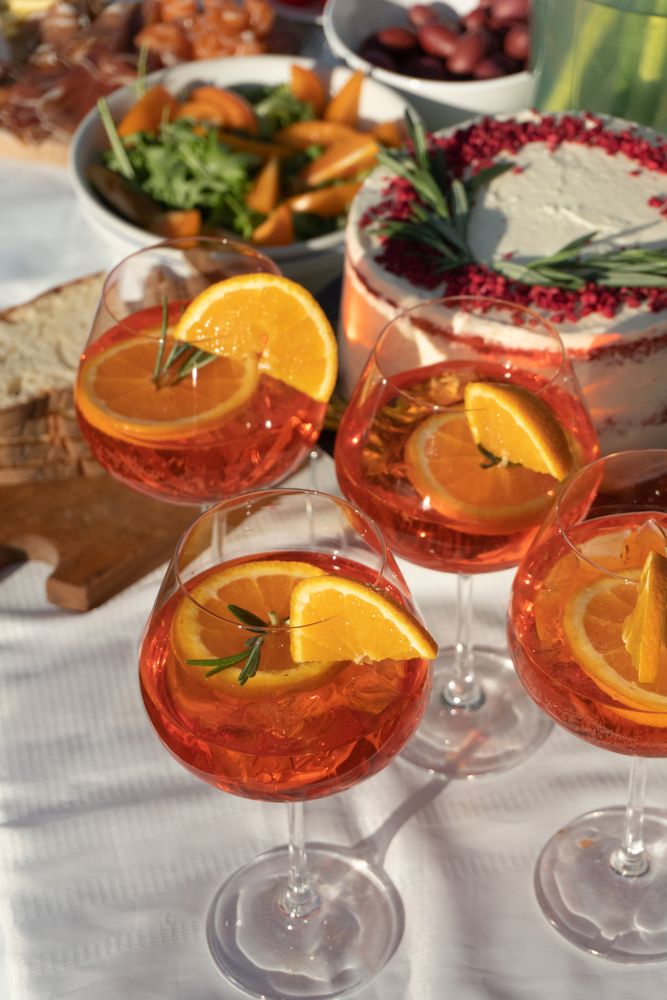 Spritz refreshing drink at the party on hot summer day served with cake, salad, bread an olives on the back ground