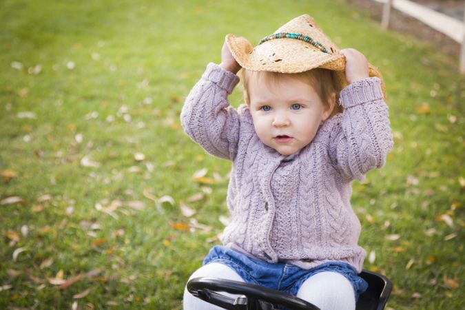 Toddler Wearing Cowboy Hat and Playing on Toy Tractor Outside
