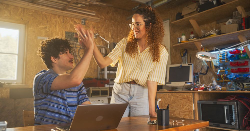 White Male Software Engineer And Hispanic Female Marketing Director Talking And Using Laptop Computer in Garage At Home.