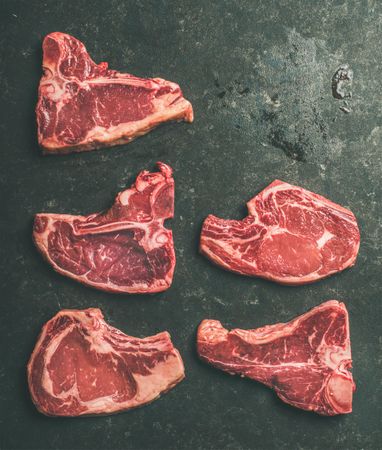 Five raw steaks on dark slab