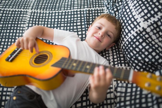 Young blonde boy playing toy guitar