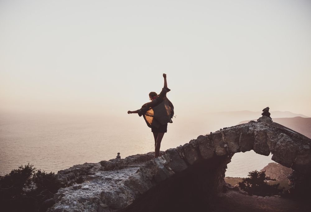Woman with arms outstretched on castle wall overlooking sea