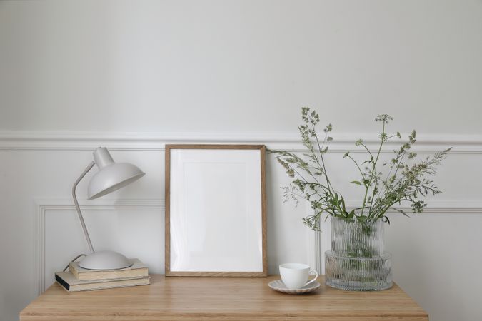 Empty vertical picture frame mockup on wooden desk with vase and branches