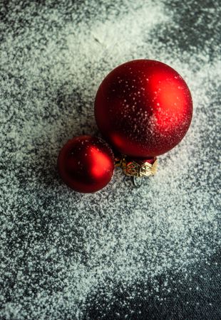 Christmas card concept with two red baubles on snowy table, vertical composition