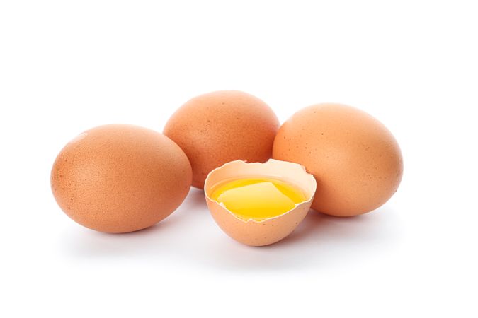 Chicken eggs and half broken egg with yolk  isolated on light background