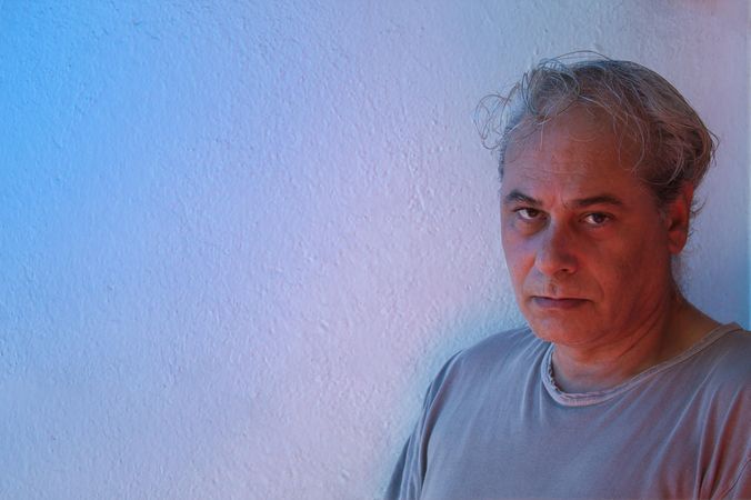 Portrait of middle aged man in gray shirt with questing look against light background in UV lit studio