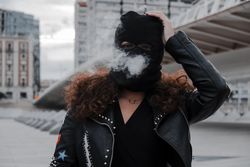 Woman in mask and jacket smoking on street
