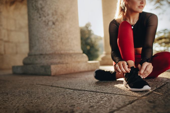Woman in fitness wear sitting on ground and tying her shoelace
