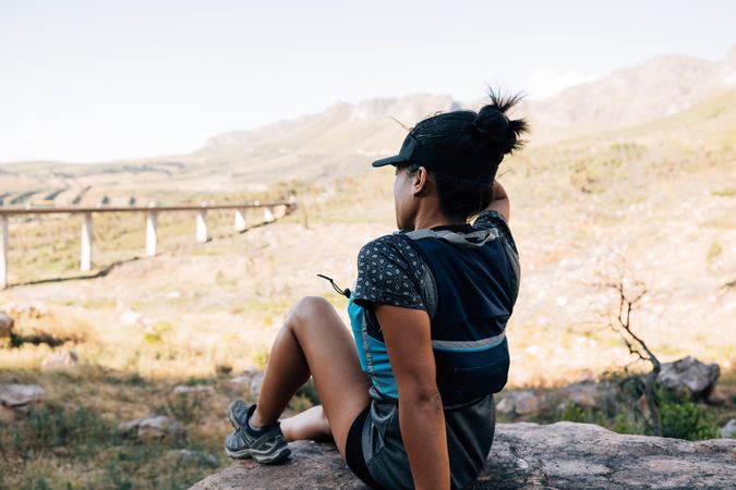 Back of female sitting on rock looking over view of a bridge in the mountains