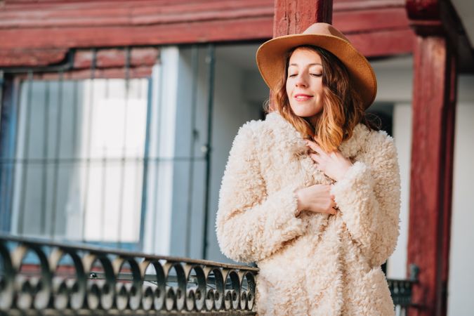 Smiling woman in warm wear standing near building and fence