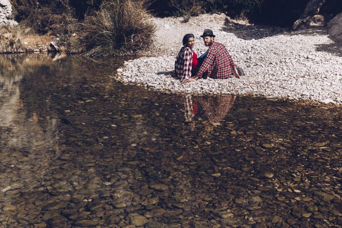 Positive woman and man resting on stone shore near river