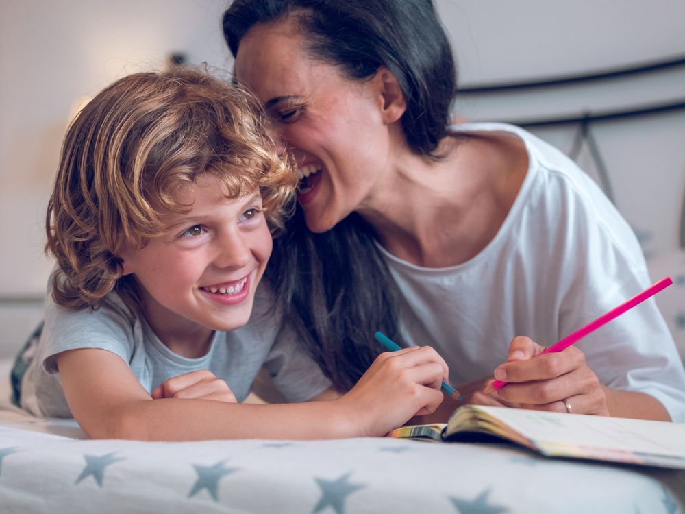 Cheerful boy and happy mother painting together lying on bed
