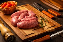 Raw sausages arranged on wooden board with rosemary and tomatoes