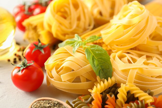 Composition with pasta, tomatoes, spices and olive oil on bright background, closeup