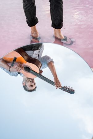 Reflection of inspired musician playing guitar at seashore in mirror