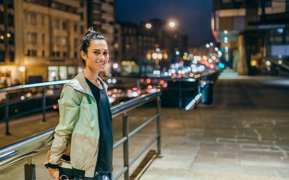 Smiling female runner stretching her legs next to banister before training at night in town