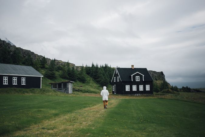 Back of man walking on grass towards house on overcast day