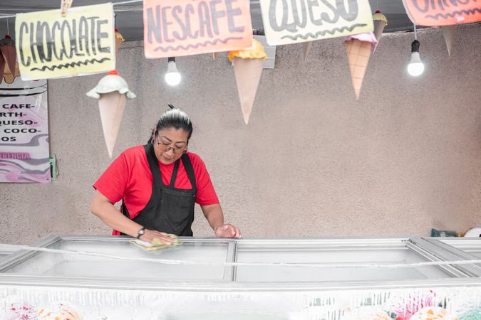 An Hispanic woman is cleaning the ice cream freezer in her street market stall