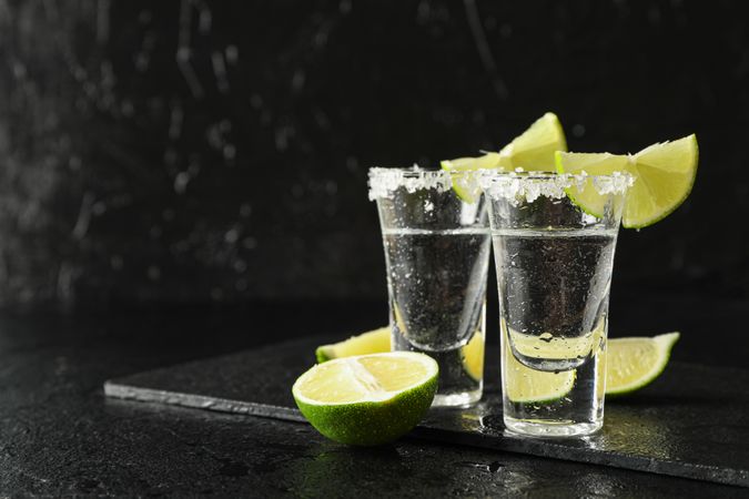 Tequila shots with salt and lime slices on dark wet background