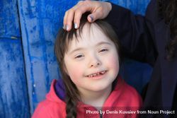 A young girl with Down syndrome smiling with a loving hand on her head 5wmWRb