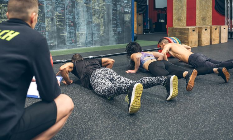 People training in the gym doing push-ups while their trainer watches them