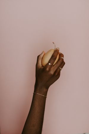 Black hand holding a pear wearing a gold bracelet and rings