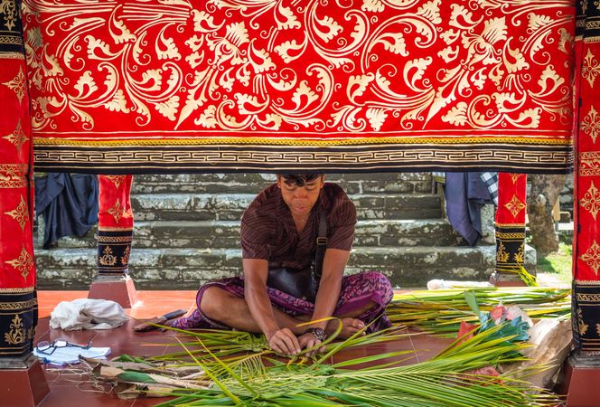 Bali, Indonesia - August, 15 2015: Indonesian man braiding palm leaves