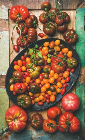 Assortment of different tomatoes in oval bowl, on wooden table, vertical composition