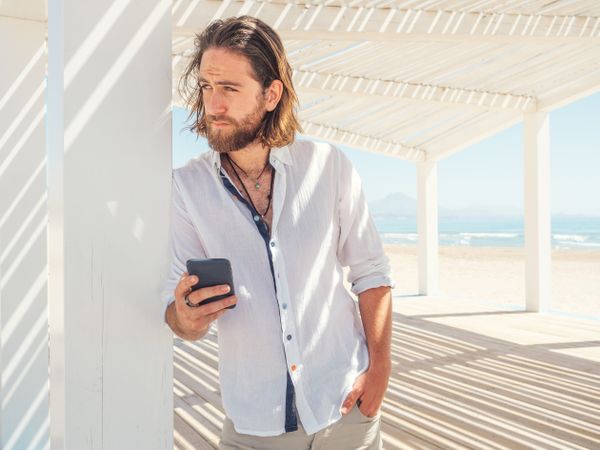 Relaxed man using smartphone in gazebo on beach