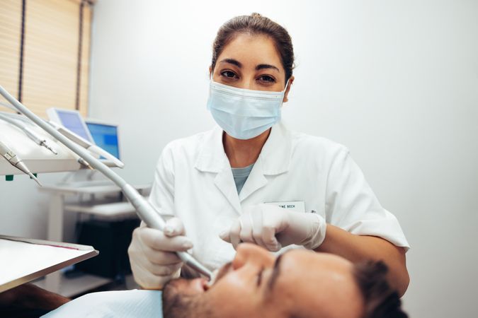 Female dentist wearing face mask looking at camera while treating a patient